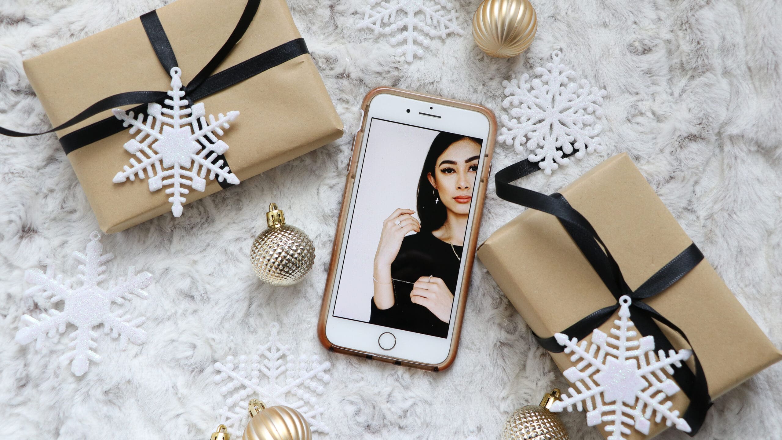 Luxury flatlay of gold-wrapped gifts on a fur backdrop with a smartphone displaying high-end jewelry photography, illustrating social media strategy for small business owners.